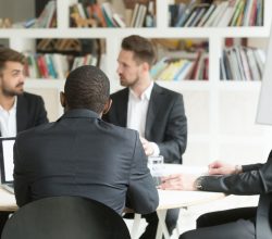 Multiethnic team of male coworkers discussing corporate plans during briefing. Businessmen having discussion about investment opportunities, new business project, company goals to improve workflow.